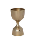 The Creative Co-op Brass Double Sided Cocktail Jigger, with an hourglass shape, wide cup, and flared base, gleams gold against a plain white background.
