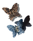 Two Fashion Hair Clips by Faire are displayed on a white background: one with brown and black leopard print, the other blue and white textured. Both are made from eco-friendly cellulose acetate with visible metal clasps casting soft shadows.