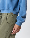 A person wearing Faire's Gwen Boyfriend Wide Leg Pant in organic cotton stands against a plain light background, with their left arm relaxed by their side and only the lower torso and upper legs visible.