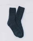The Faire Wool Speckled Knit Socks, thick and dark-colored with a ribbed cable-knit pattern, are laid flat on a light surface.