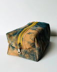 The Dyed Toiletries Bag by Faire is a rectangular, hand-dyed cotton pouch with a yellow zipper and blue-brown tie-dye pattern—ideal for organizing your desk.