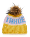 The Faire Knit Ski Hat is a luxury yellow merino wool beanie with pastel pink and blue stripes, “TAHOE” in blue letters, a folded brim, and a large brown faux fur pom pom on top.