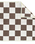 A brown and white checkerboard waffle weave microfiber washcloth with a textured, high-absorbent surface is shown. One corner is folded to reveal the reverse side and a white tag with the brand name "Faire" is visible.