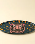 The Tiger Spot Tray by Indaba is an oval accent tray with a dark base, orange spots, and a central pink tiger face—ideal for adding decorative flair to any space.