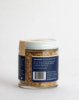 A small glass jar with a white lid holds Faire's White Truffle Salt, a coarse, light brown blend. The label lists "Ingredients: Sea salt, white truffle" and provides product details plus the manufacturer's address.