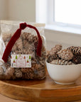 Faire's Christmas Potpourri White Cones come in a clear bag with a red ribbon and holiday label, offering frosted pine cones that bring an earthy fragrance to your festive decor.