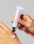 A hand dispenses Faire Eye Opener - Smoothing & Brightening Cream, a white formula with a metal applicator tip, onto the back of another hand—ideal for puffiness and dark circles—all set against a neutral background.