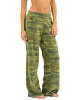 A person stands barefoot in loose, green camouflage Aviator Nation 5 Stripe women’s wide leg pocket sweatpants with an elastic waistband and a small embroidered logo by the left pocket. The image is cropped from shoulders to feet.