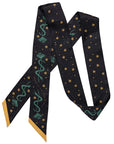 The Faire Twilly Scarf features black silk with yellow star patterns, green caduceus symbols, and yellow-tipped ends—arranged in a zigzag shape, it's an ideal gift for any occasion.