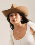 A woman models the Faire Charlie Western Hat, paired with a white tank top, hoop earrings, and a long necklace, looking calmly at the camera against a neutral background.