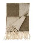 The Indaba Checkerboard Throw in Taupe features large beige and brown checkered squares with cream fringe edges. One corner is flipped over, revealing the stylish reverse side of this modern throw blanket.