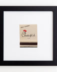 A framed picture hangs on a white wall. It features a Chick-fil-A sauce packet in the center. The packet has the Chick-fil-A logo, a red chicken head, and the text "TREAT YOURSELF" at the top. The black frame contrasts beautifully with its clear acrylic cover and white background, making it an exceptional piece of art. This is all elegantly captured in the Art Square Blk Frame by Match South.