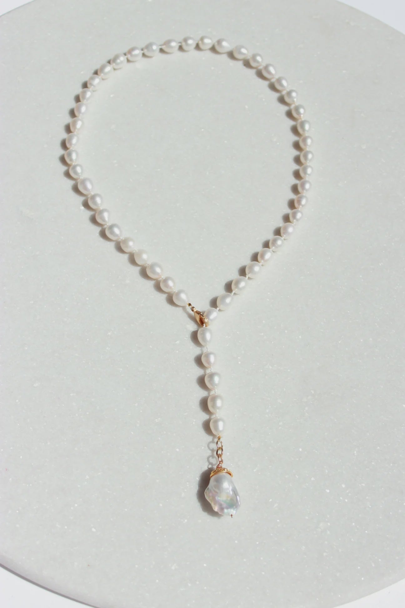 A hand-crafted Classic Pearl Necklace from Bittersweet Designs with a pendant displayed against a light gray background, arranged in a teardrop shape. The pendant features a larger, iridescent pearl dangling from the center.