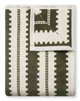 The Faire Collins Stripe Blanket features olive green and cream wavy stripes with a geometric zigzag design, smooth soft texture, and finished white edges—ideal for cozying up in layered fall spaces.