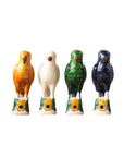 Four Parrot Small whistles by Blue Ocean Traders stand in a row in orange, white, green, and dark blue colors on green and yellow bases with a front hole—evoking Jingdezhen hand-painted porcelain artistry.