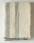 The Faire Cozy Stripe Throw, a cream-colored wool-blend with black vertical stripes and stitched edges, is folded neatly on a white surface.