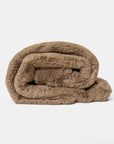 The Cuddle Blanket by Cozy Earth, an ultra-plush light brown faux fur throw, is neatly rolled up on a plain white background.
