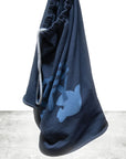 The FreeCity Cutoffs bag by Free City (sparrow, LLC) is a dark blue French terry drawstring with a light blue bird and branch design, displayed against a white background and gray concrete floor.