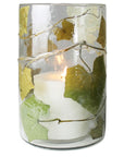 The HomArt Enameled Hurricane / Ivy is a glass candle holder with a white candle, featuring pressed green and yellow leaves and embossed branches—a charming luminary for your garden.