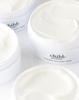 Open jars of Faire’s Child Rich Body Creme, filled with smooth, creamy white luxurious cream, are arranged close together on a white surface.