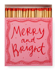 A pink square box of Faire Matches features red-tipped matches and a lid with "Merry and Bright" in bold red script, surrounded by a dotted border—a unique design from Faire.