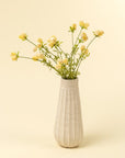 The Indaba Dandelion Pom Pom Spray features delicate yellow blooms with thin green stems in a white fluted vase, set against a pale yellow background—an ideal accent decor piece for any room.
