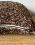 The Faire Adah Coco Wool & Linen Pillow, featuring a textured stonewash finish and visible silver zipper, rests on a wooden surface against a plain light-colored wall.