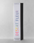 Tall, white rectangular box of Faire Incense Sticks labeled “DESERT FLEUR” in rainbow letters with patchouli notes stands upright on a neutral gray background, casting a shadow to the right.