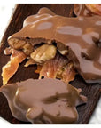 Close-up of Faire LC Longhorns Milk Chocolate 6oz—decadent caramel and Texas pecan clusters—on a dark wood surface, with one split to show gooey caramel and crunchy pecans inside.