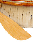 A close-up of the Creative Co-op Brie Baker with Bamboo Spreader, featuring a brown-glazed, speckled ceramic bowl—perfect for serving with any farmhouse-style canapé knives or as a charming addition to your bakeware.