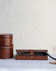 Two round cognac leather Creative Co-op DG0045 boxes are stacked beside a rectangular MDF & leather box with its lid open, revealing black beads and rope inside, all set on a light surface against a neutral background.