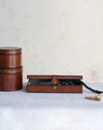 On the left, two cognac leather containers are stacked. On the right, a Creative Co-op Leather Box Snap Closure made of MDF & leather is open, displaying a black beaded tassel necklace on a light-colored surface.