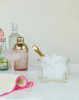 A marble countertop displays spirits, a cocktail glass, a gold shaker, a textured towel, and the Creative Co-op Glass Ice Bucket with Tongs featuring a textured design and a gold-finished handle.