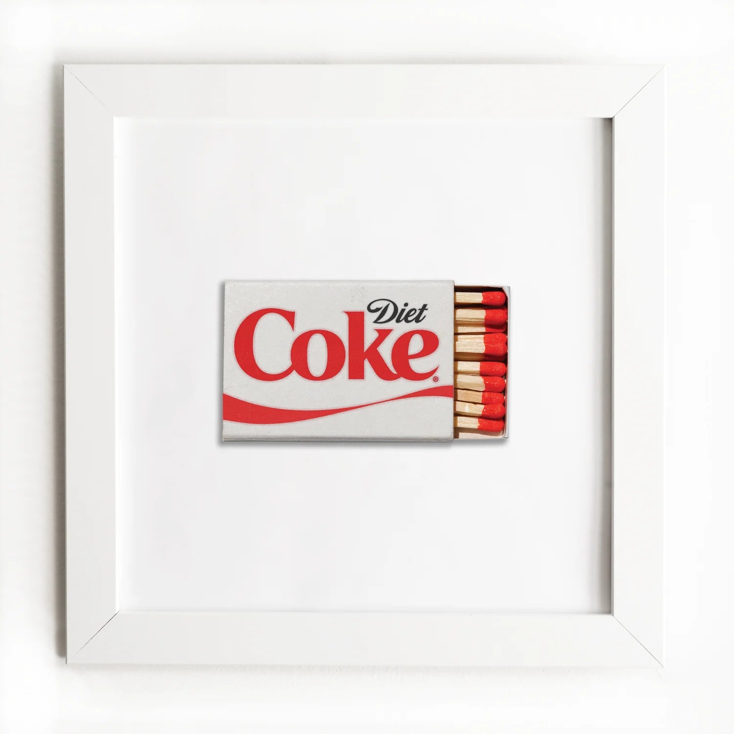 A framed artwork showcasing a miniature Diet Coke can label partially wrapped over a small matchbox with red-tipped matches, all against a pure white background in Match South style using the Art Square White Frame.