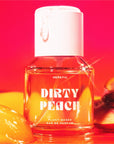 A clear bottle of Heretic 50ML Perfume by Faire, labeled "Dirty Peach," rests against a vibrant red and orange background with peach slices and syrup, suggesting a sensual fragrance featuring sandalwood vanilla notes.