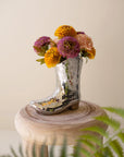 Kalalou, Inc’s Ceramic Disco Boot Vase, shaped like a silver disco ball boot, bursts with colorful flowers on a round wooden stool—an eye-catching quirky cowgirl gift.