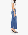 A woman stands sideways against a white background wearing Mother’s The Mid Rise Rambler Zip Ankle Fray jeans, a white short-sleeve crop top, and dark high-heeled sandals.