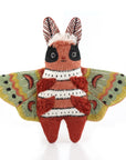 The Faire Moth Embroidery Kit features a plush toy moth with wide, colorful green and yellow wings, a striped red and white body, and large black eyes—perfect for Kiriki Patterns fans. Displayed upright on a white background.
