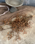 The Faire 22'' Faux Seeded Baby's Breath Bunch is displayed on a textured beige surface next to a gray stone pedestal and sheer taupe fabric, with delicate faux stems adding charm.