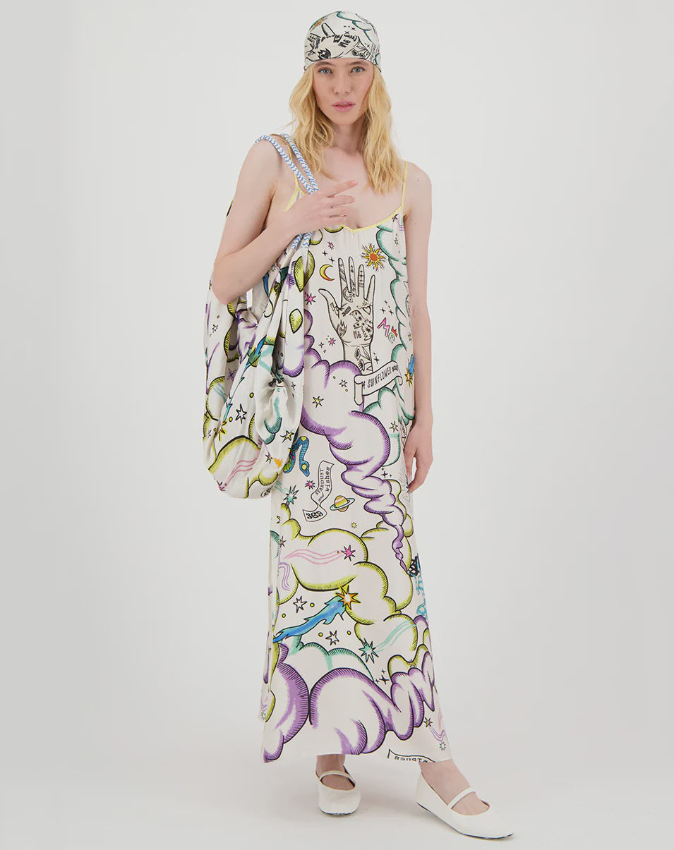 A woman stands against a white background wearing the Me369 Olivia Camisole Dress featuring a colorful Enlightenment pattern, with a matching headscarf, white shoes, and a large coordinated shoulder bag.