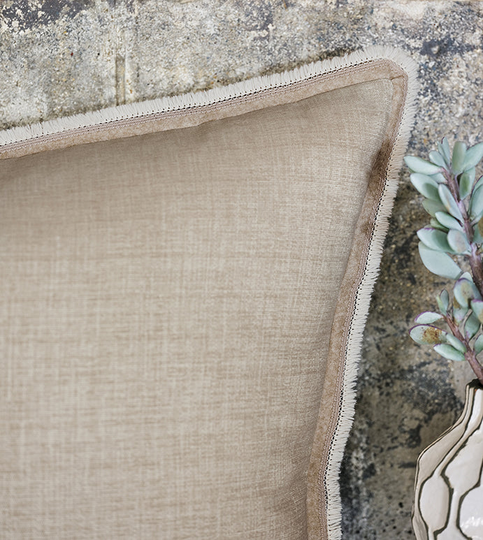 Close-up of a Eastern Accents Aldrich Brush Fringe 27x27" beige linen pillow with zigzag stitch edging on a rustic stone surface at a bungalow in Scottsdale, Arizona, alongside a succulent plant in a ceramic pot.