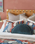 A stylishly decorated bedroom corner in a Scottsdale bungalow featuring a Moab Graphic 27x27" bedspread from Eastern Accents with an artistic headboard against a soft coral wall, adorned with decorative pillows in various patterns and a bedspread with abstract design.