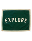 The Oxford Pennant Explore Camp Flag 18x24 features bold white "EXPLORE" lettering on green with a beige border and four metal grommets—ideal décor for adventurers and outdoor enthusiasts.