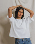 A woman with long dark hair wears the Perfectwhitetee French Terry SS Loose Sweatshirt and blue jeans, standing before a light fabric backdrop with her arms raised above her head.