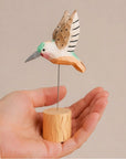 Faire Hand-Painted Brown Carved Hummingbird on wire and wooden base held in hand.