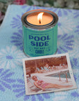 A lit G&W Soy Candle by Faire sits on a blue and purple patterned towel next to a vintage photo of a woman in sunglasses and a swimsuit, evoking nostalgic joy by the pool.