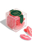 The Faire Christmas Candy Cube showcases pink, sugar-coated gummy lips as festive holiday treats. Two gummies sit outside the clear, branded box for a charming seasonal display.