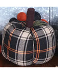 The Faire Pumpkin is a farmhouse decor piece with black, white, and orange plaid fabric, a brown stem, and round felt balls on top—a charming autumn ornament for your home against any metallic background.