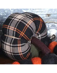 The Pumpkin by Faire is a plaid, pumpkin-shaped autumn ornament in black, white, and orange fabric, accented with matching felted balls—perfect for cozy farmhouse decor on a metallic background.