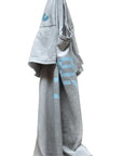 A light gray Free City FC thedoingofitis... SS Tee with blue graphics hangs on a hook against a white background. Casually draped, it shows off its custom sunfade dye, with one sleeve facing out and the lower hem hanging down.
